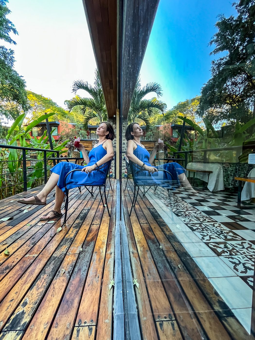 Mujer relajada en la terraza de madera, reflejo en el cristal y vegetación al fondo